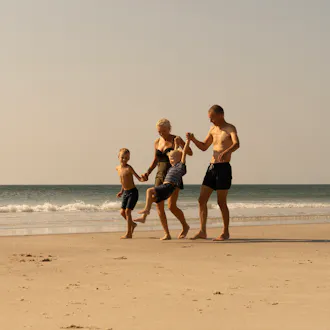 Familie på stranden nær sommerhus. De går langs vandkanten, og børnene griner.