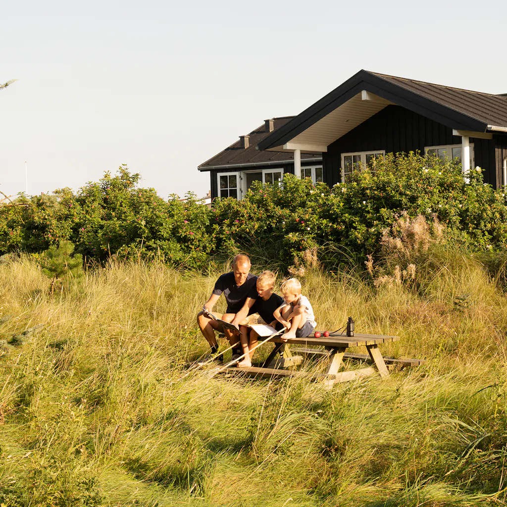 Forældre og børn sidder i naturgrønt område bag sommerhuset. Hyggestund og fordybelse.